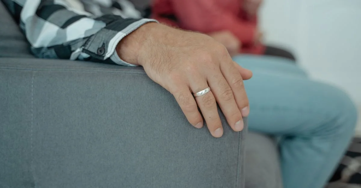 Une vue rapprochée de mains adultes reposant sur un canapé, portant une bague de mariage à l'intérieur.
