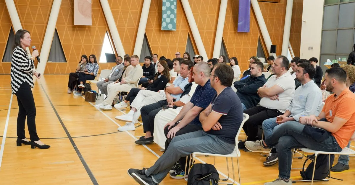 Un orateur s'adresse à un public attentif dans une salle moderne au décor triangulaire.