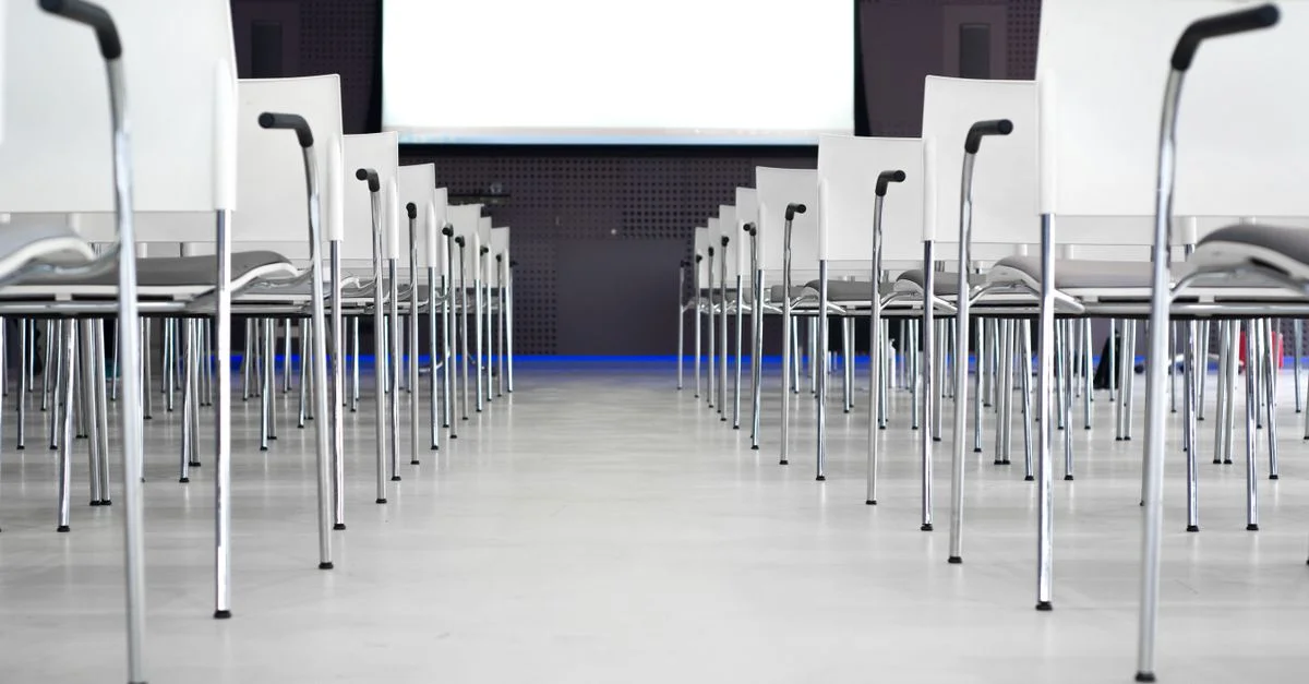 Salle de conférence moderne vide avec des chaises blanches en rangées, prête pour une présentation.