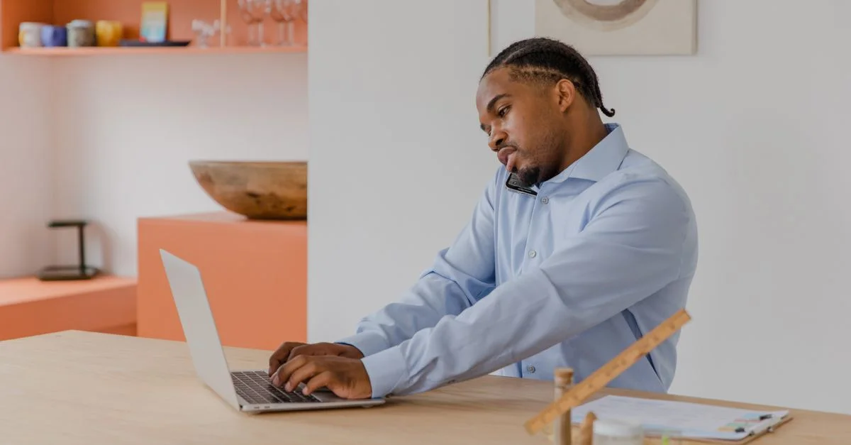 Homme d'affaires concentré utilisant un ordinateur portable et un téléphone simultanément, travaillant dans un espace de bureau moderne.